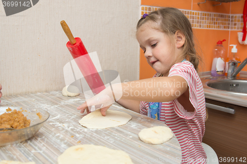 Image of The girl rolls the dough with a rolling pin for pies