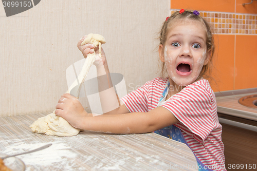 Image of The girl tears off a piece of dough for pies and happily looks into the frame