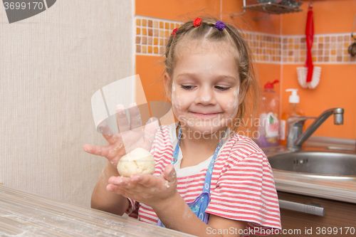 Image of Happy little girl girl sculpts a pie at the kitchen table