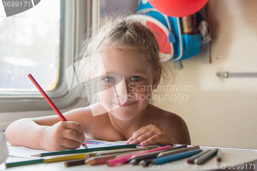 Image of Happy little girl drawing with pencils at a table in a train