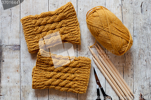 Image of wool yellow legwarmers, scissors, knitting needles and yarn 