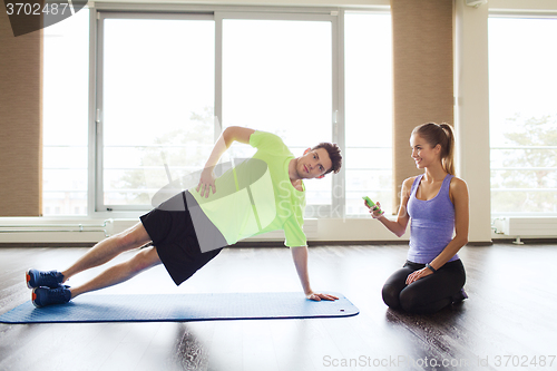 Image of man and woman doing plank exercise on mat in gym