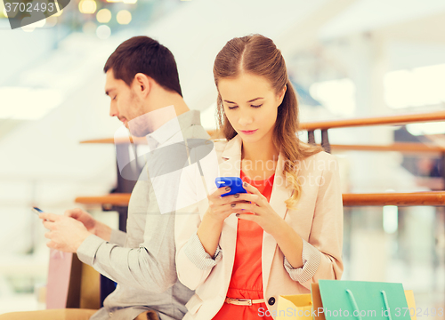 Image of couple with smartphones and shopping bags in mall