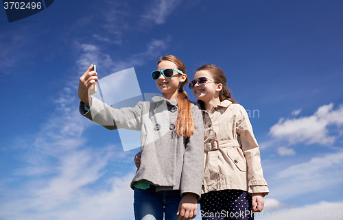 Image of happy girls with smartphone taking selfie outdoors