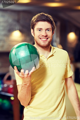 Image of happy young man holding ball in bowling club