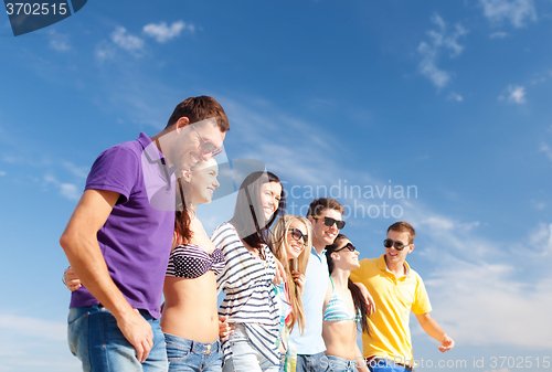 Image of group of happy friends walking along beach