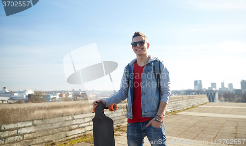 Image of smiling teenager with longboard on street