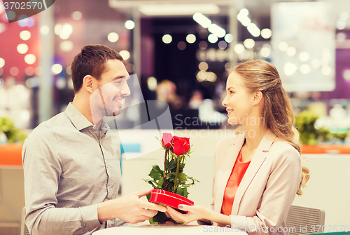 Image of happy couple with present and flowers in mall