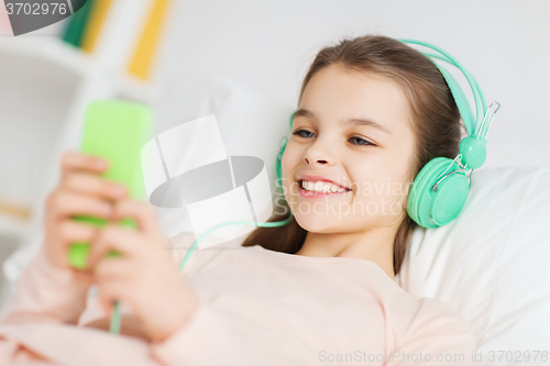 Image of happy girl lying in bed with smartphone at home