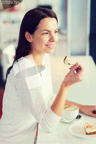 Image of smiling young woman with cake and coffee at cafe
