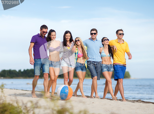 Image of group of happy friends walking along beach