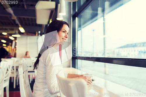 Image of smiling young woman drinking coffee at cafe