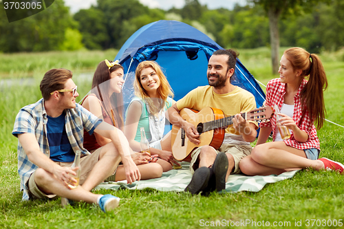 Image of happy friends with drinks and guitar at camping