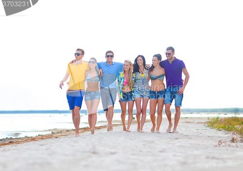 Image of group of happy friends walking along beach