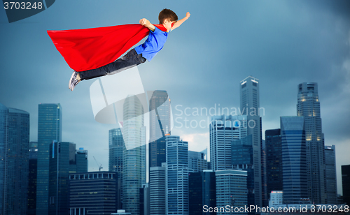 Image of boy in red superhero cape flying over city