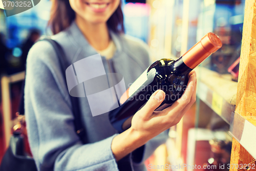 Image of happy woman choosing and buying wine in market