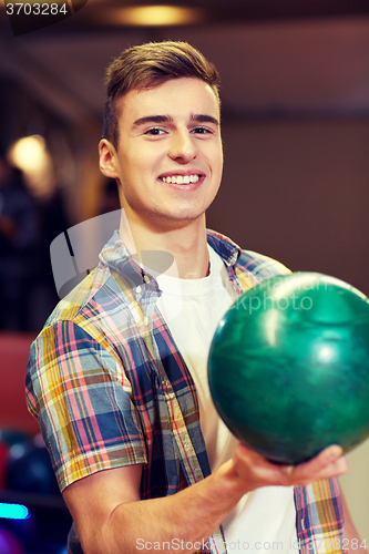 Image of happy young man holding ball in bowling club