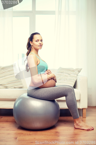 Image of happy pregnant woman exercising on fitball at home