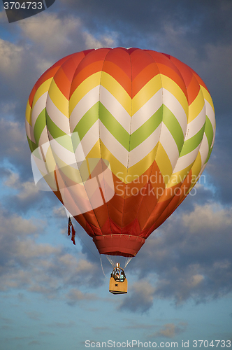 Image of Orange and yellow hot-air balloon floating among clouds