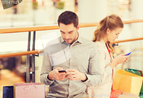 Image of couple with smartphones and shopping bags in mall