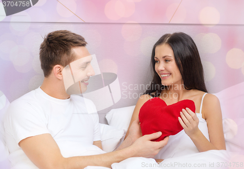 Image of smiling couple in bed with red heart shape pillow