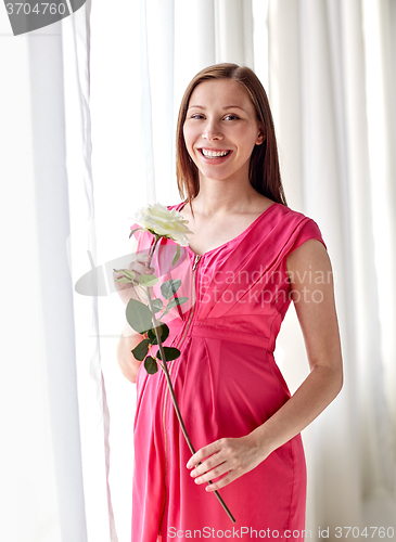 Image of happy pregnant woman with rose flower at home