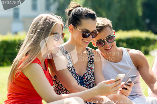 Image of smiling friends with smartphones sitting in park