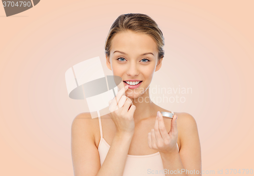 Image of smiling young woman applying lip balm to her lips