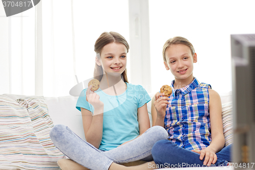 Image of happy girls watching tv and eating cookies at home