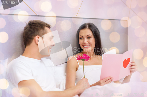 Image of smiling couple in bed with postcard and flower