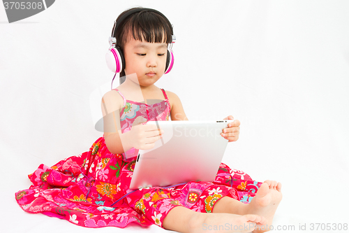 Image of Chinese little girl on headphones holding tablet