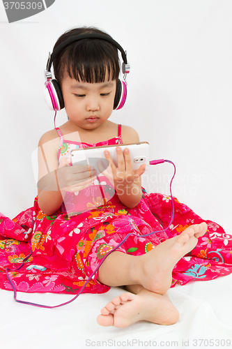 Image of Chinese little girl on headphones holding mobile phone