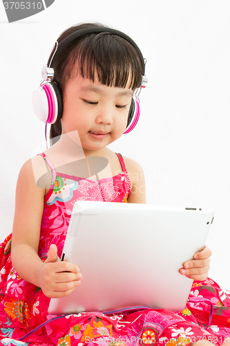 Image of Chinese little girl on headphones holding tablet