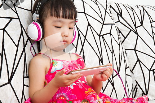 Image of Chinese little girl on headphones holding mobile phone