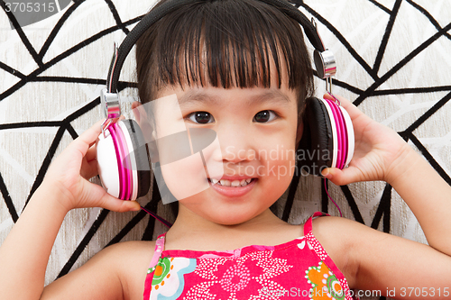 Image of Chinese little girl on headphones holding mobile phone