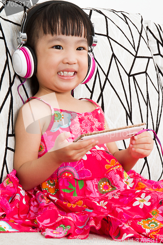 Image of Chinese little girl on headphones holding mobile phone