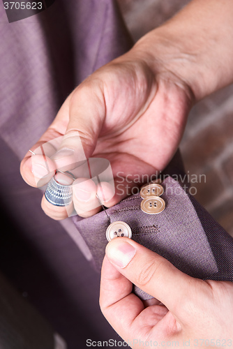 Image of dressmaker sews a button on jacket