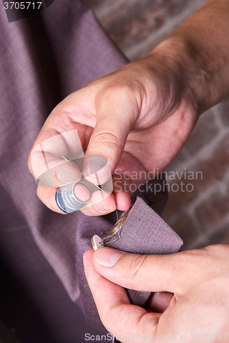 Image of dressmaker sews a button on jacket