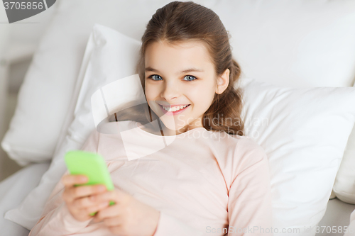 Image of happy girl lying in bed with smartphone at home