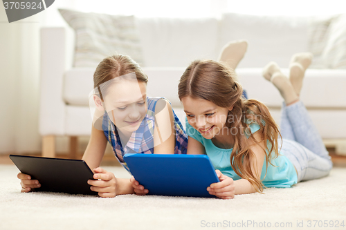 Image of happy girls with tablet pc lying on floor at home