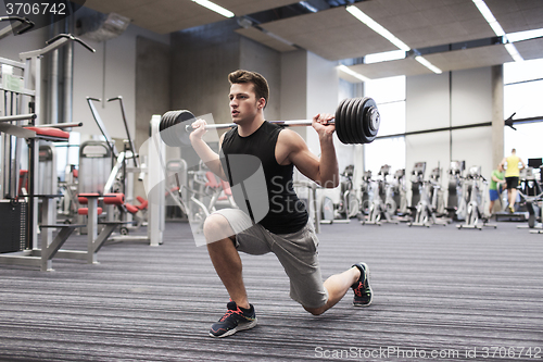 Image of young man flexing muscles with barbell in gym