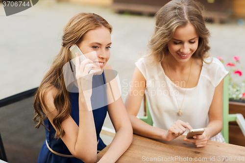 Image of happy young women with smartphones at outdoor cafe