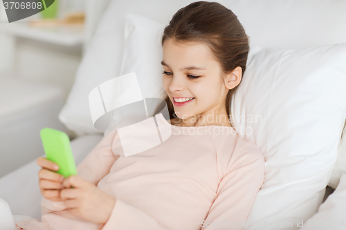 Image of happy girl lying in bed with smartphone at home