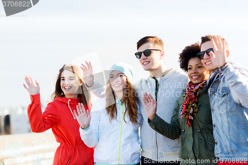 Image of happy teenage friends waving hands on city street