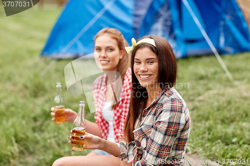 Image of happy young women with tent and drinks at campsite