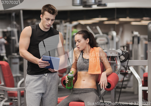 Image of smiling young woman with personal trainer in gym