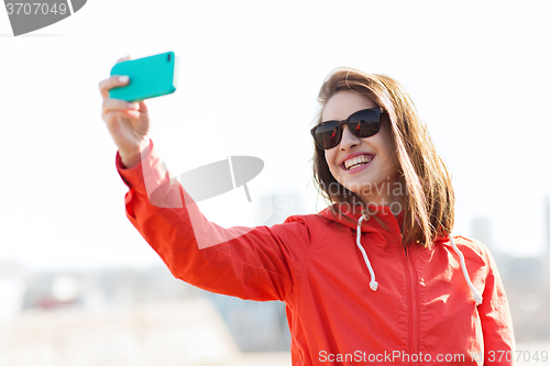 Image of smiling young woman taking selfie with smartphone