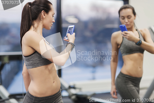 Image of woman with smartphone taking mirror selfie in gym