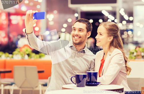 Image of happy couple with smartphone taking selfie in mall