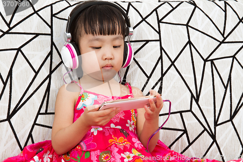 Image of Chinese little girl on headphones holding mobile phone